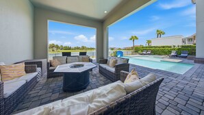 An outdoor patio with wicker furniture, a fire pit, and a view of a swimming pool and distant buildings. - Upscale Villa with Home Theater at Reunion (Kissimmee)