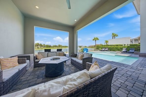 An outdoor patio with wicker furniture, a fire pit, and a view of a swimming pool and distant buildings. - Upscale Villa with Home Theater at Reunion (Kissimmee)