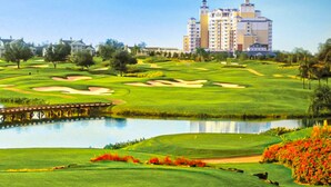 Un parcours de golf avec un plan d’eau, un pont et, au loin, un grand bâtiment d’hôtel.