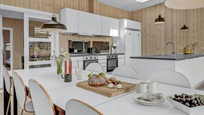 Een moderne keuken met witte kasten, een accentmuur van hout en een eethoek met witte stoelen en een houten tafel.