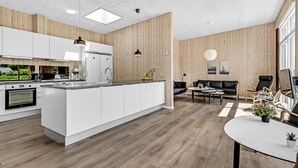 Een moderne keuken met witte kasten, een centraal eiland en een eethoek met een leren zwarte bank en salontafel.