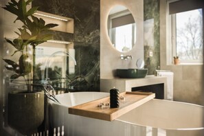 Een moderne badkamer met een marmeren wastafel, een grote spiegel en een plant in een pot.