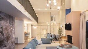 Een ruime woonkamer met een hoekbank, een eettafel met stoelen, een aan de muur bevestigde televisie en een open haard.