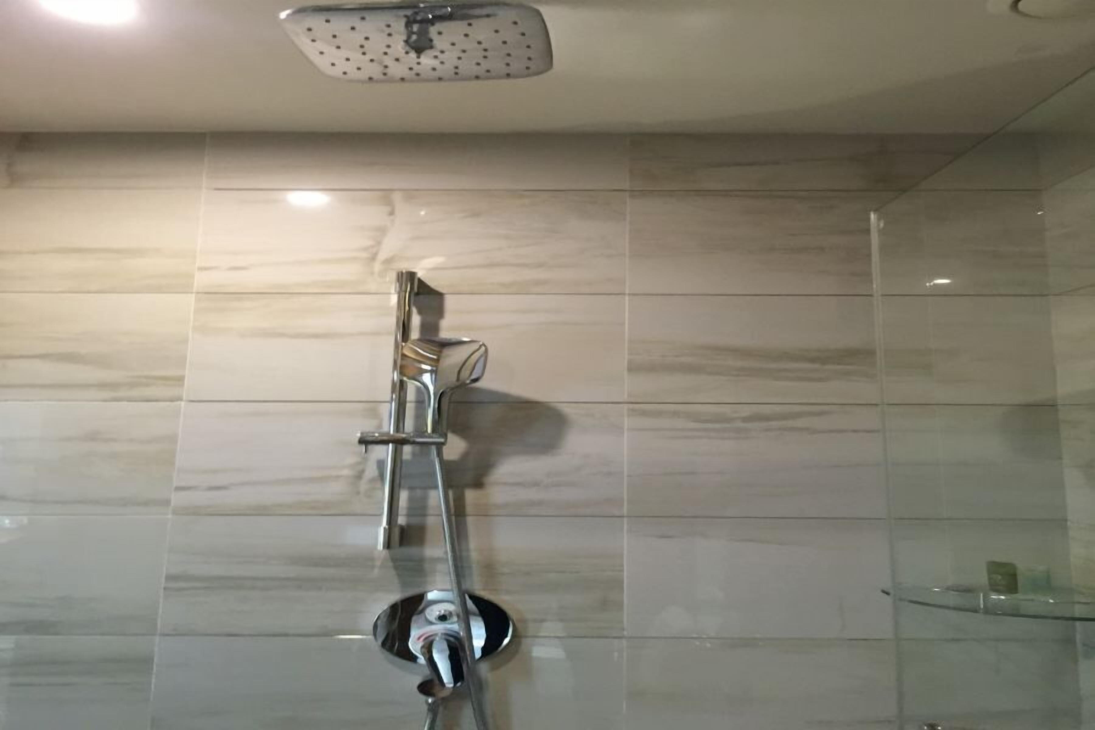 A modern bathroom with a chrome showerhead, a glass shelf, and marble tiles.