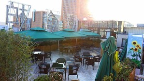 An outdoor patio area with tables and chairs, covered by green umbrellas, and surrounded by buildings. - Melody Hotel (Longyan)