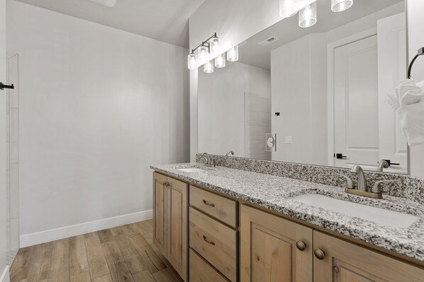 Une salle de bain moderne avec un lavabo sur un plan de travail en granit, des meubles en bois et un grand miroir.