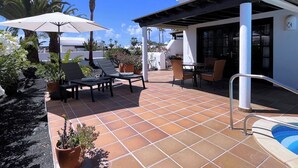 A patio with outdoor seating, a pool, and a covered area with a grill.