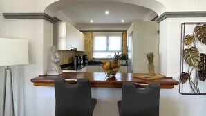 A modern kitchen with a central island, two bar stools, a Buddha statue, and a fruit bowl.