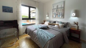 A bedroom with a bed, a desk, a chair, a window, and a painting on the wall.