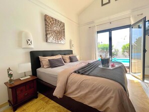 A bedroom with a bed, bedside table, and a view of a swimming pool.