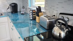 A modern kitchen with a glass countertop, a coffee maker, a toaster, a kettle, and a knife block.