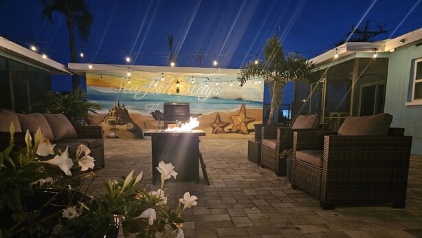 An outdoor patio area with wicker furniture, a barbecue grill, and a mural of a beach scene.