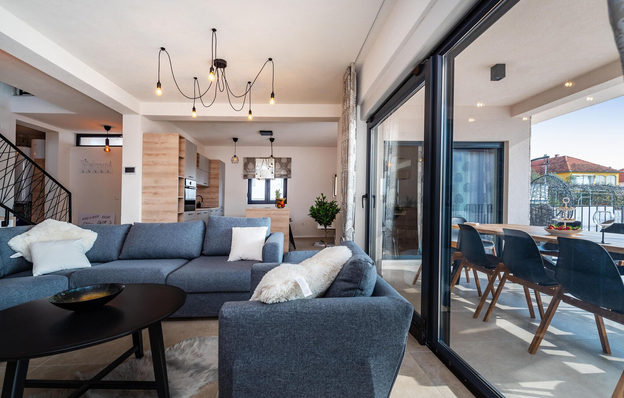 A modern living room with a large grey sectional sofa, a black coffee table, and a dining area with wooden chairs and a glass table.