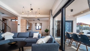 Een moderne woonkamer met een grote grijze modulaire bank, een zwarte salontafel, en een eethoek met houten stoelen en een glazen tafel.