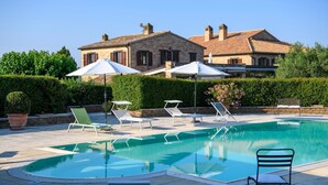 Ein Swimmingpool mit Liegestühlen und Sonnenschirmen, umgeben von einem Gebäude mit Steinwänden und einem Ziegeldach.