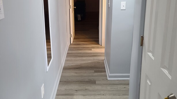 A hallway with light gray walls, wooden flooring, and a white door with a keychain. - Harrison Hotel Unit D
Pet Friendly 
Ground Level Unit (Garden City Beach)