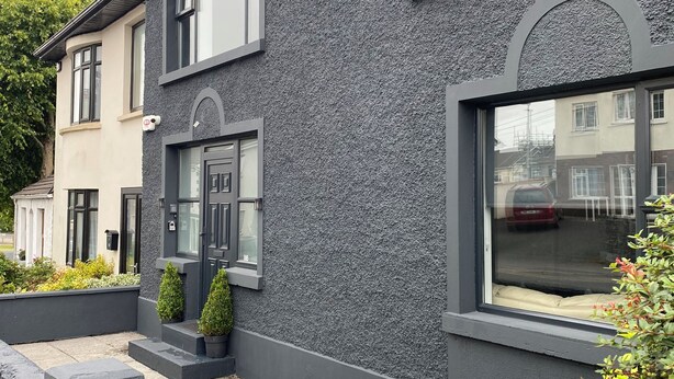 Et moderne hus i to etager med en struktureret grå facade, store vinduer og en tydelig dør.