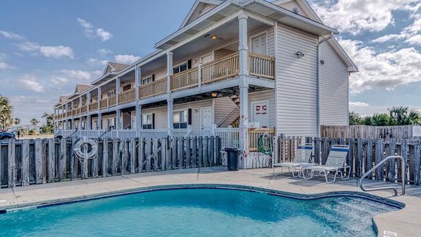 Ein zweistöckiges Motel mit Poolbereich, Holzterrasse und einem eingezäunten Schwimmbecken.