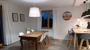 Un coin repas avec une table et des chaises en bois, un luminaire suspendu et une horloge au mur.