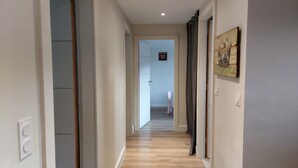 Un couloir doté d’un plancher en bois, une porte sur la gauche et une œuvre d’art accrochée au mur sur la droite.