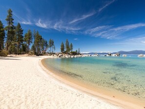 Ein sandiger Strand mit klarem türkisblauem Wasser, umgeben von Bäumen und Felsen.