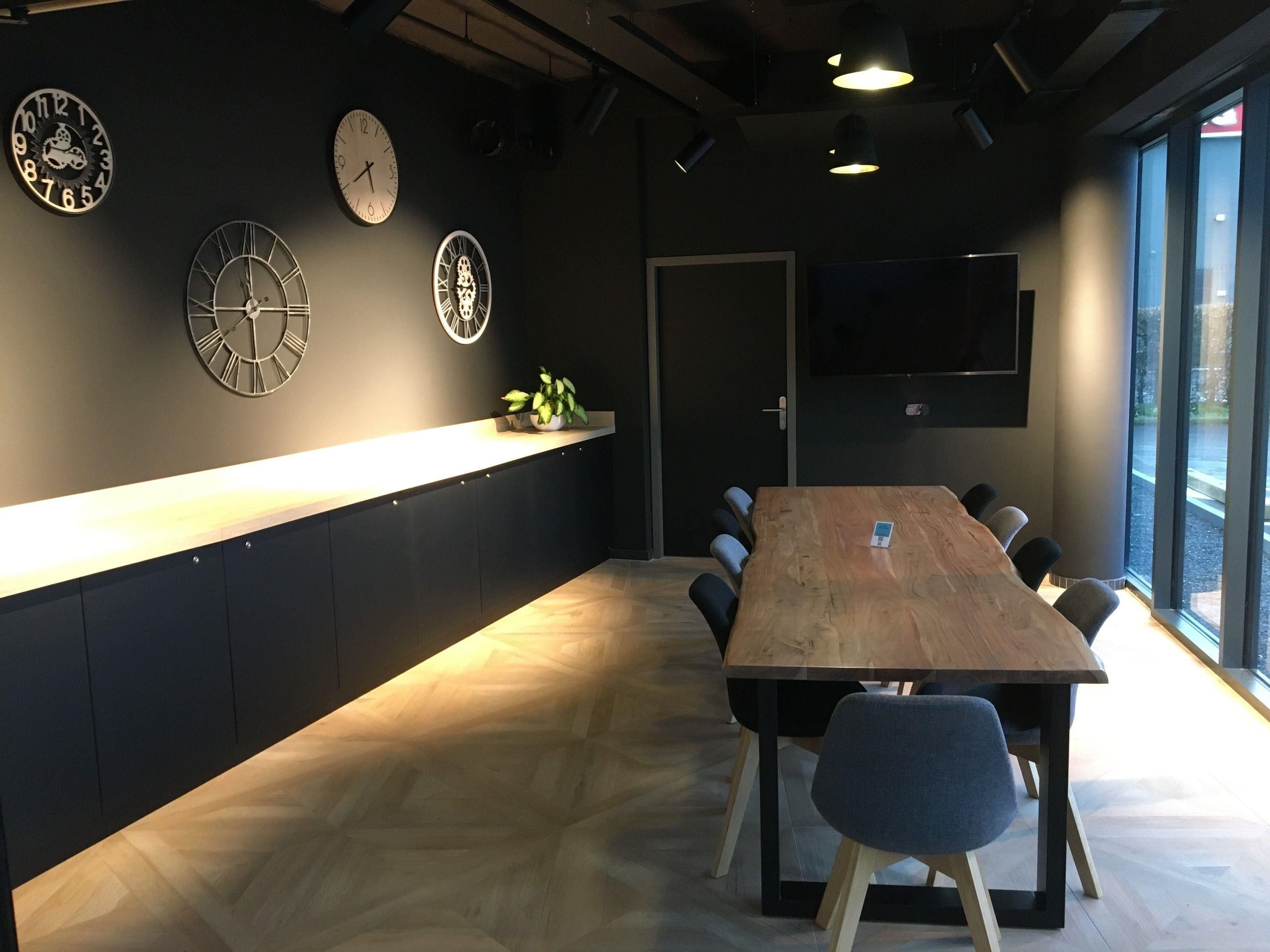 A conference room with a long wooden table, multiple chairs, a clock on the wall, and a TV mounted on the wall.