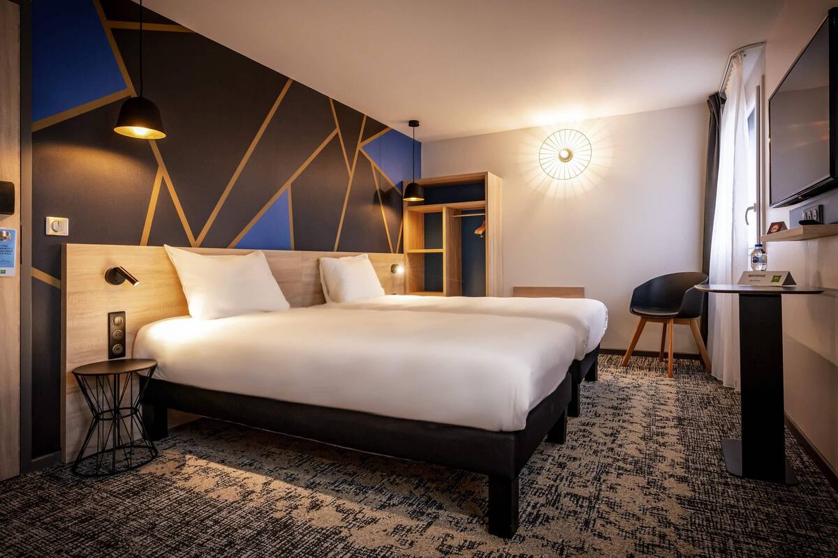 A hotel room with a large bed, bedside tables, a desk, and a mirror.