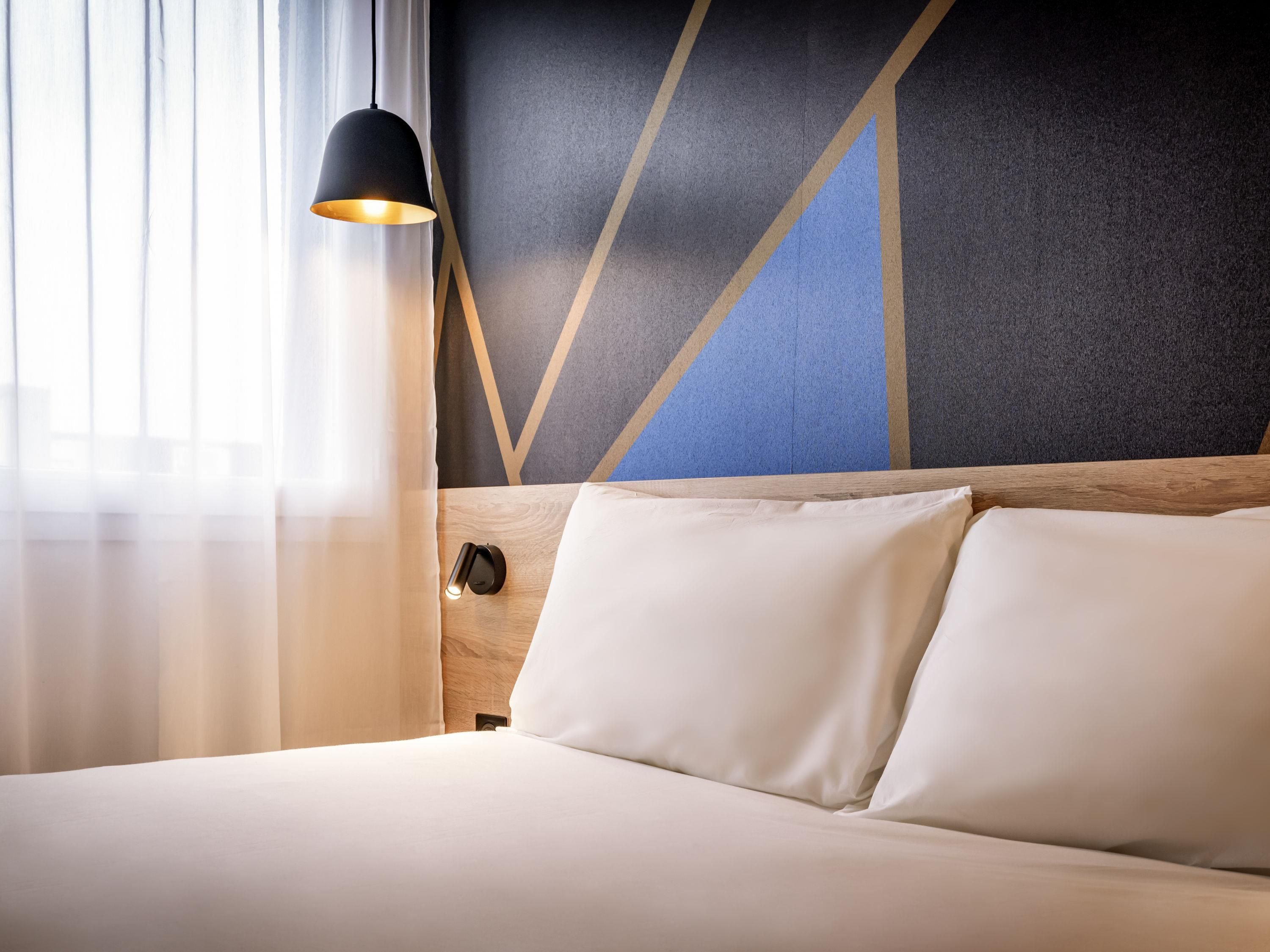 A hotel room with a bed, a nightstand, a lamp, and a wall with geometric patterns.