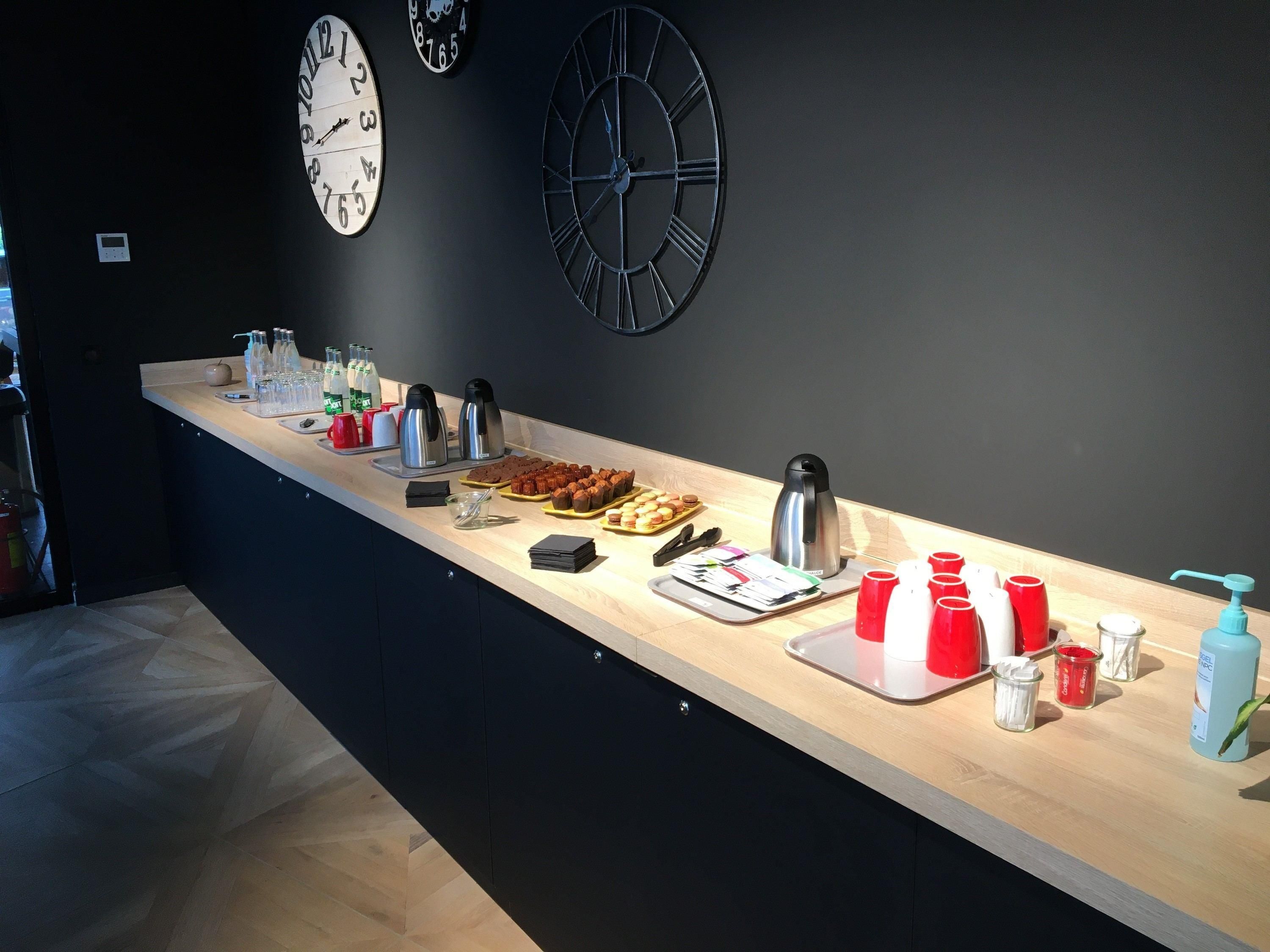 Uma mesa de pequeno-almoço com máquinas de café, chávenas e pastelaria.