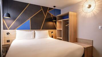 A modern hotel room with a large bed, built-in wardrobe, and a unique geometric wall design.