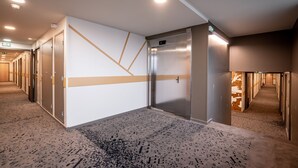 Un vestíbulo de hotel con diseño moderno, que cuenta con un ascensor central, varias puertas y una alfombra estampada.