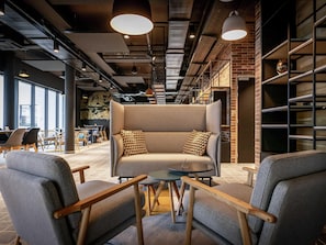 A modern interior with a sofa, chairs, and a brick wall. - Ibis Styles Valenciennes Petite Foret (Petite-Foret)