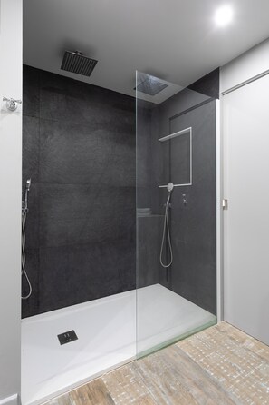 A modern shower area with a glass partition, a handheld showerhead, and a wall-mounted control panel. - Sunrise 21 (Collectivité de Saint-Martin)