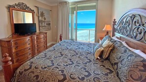Un dormitorio con cama, cómoda, televisor, ventilador de techo y vista al mar.