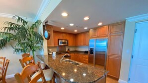 Cocina con encimeras de granito, armarios de madera y electrodomésticos de acero inoxidable, además de un comedor con sillas de madera.