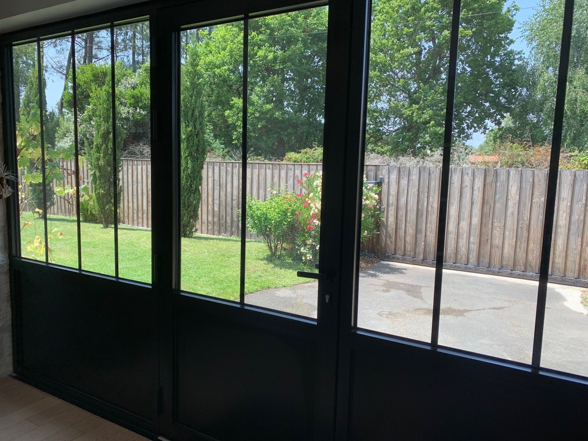 A view through a large window with a wooden fence and greenery outside.