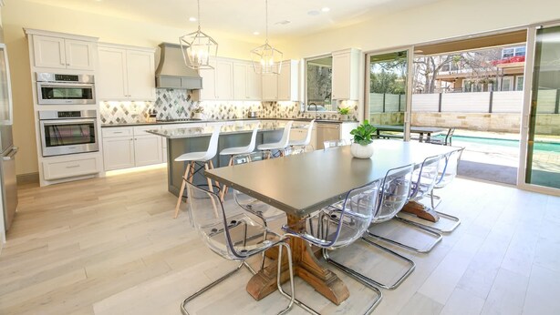 A modern kitchen with white cabinets, stainless steel appliances, a large island with chairs, and a view to the outside. - Waterfront House | Heated Pool* | Pet Friendly (Horseshoe Bay)