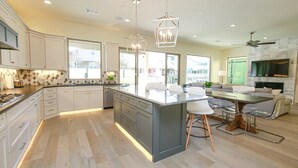 A modern kitchen with a central island, pendant lighting, and a dining area with a sofa and chairs. - Waterfront House | Heated Pool* | Pet Friendly (Horseshoe Bay)
