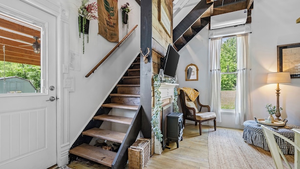 A staircase with wooden steps and a black handrail, leading to a room with a window, a lamp, and a chair.