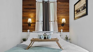 A neatly made bed with a tray, two wall-mounted lamps, a small plant, and a framed picture on the wall.