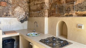 A kitchen with a stone wall, a gas stove, a sink, and a small window. - DAMMUSO to REKALE (Rekhale)