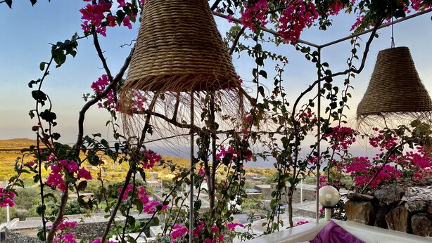A terrace with a view of a hilly landscape, featuring a wicker hanging chair and a cushioned seating area with striped pillows. - DAMMUSO to REKALE (Rekhale)