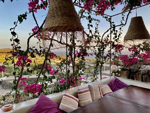 A terrace with a view of a hilly landscape, featuring a wicker hanging chair and a cushioned seating area with striped pillows. - DAMMUSO to REKALE (Rekhale)