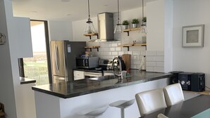 Una cocina moderna con una isla central, taburetes de bar, una mesa de comedor y vistas al exterior.