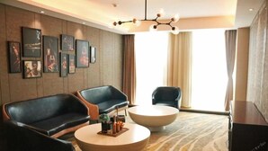 A modern hotel room with a black leather sofa, two round coffee tables, and a large window with curtains.