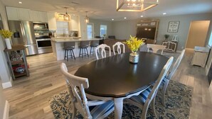 Una cocina moderna con electrodomésticos de acero inoxidable, un comedor con mesa de madera oscura y sillas blancas, y un tapete estampado en el suelo.