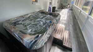 Un área de spa con hidromasaje, terraza de madera y amplios ventanales a lo largo.