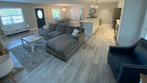 Una sala de estar amplia con un sofá seccional gris, una mesa de centro y una zona de comedor con mesa y sillas.
