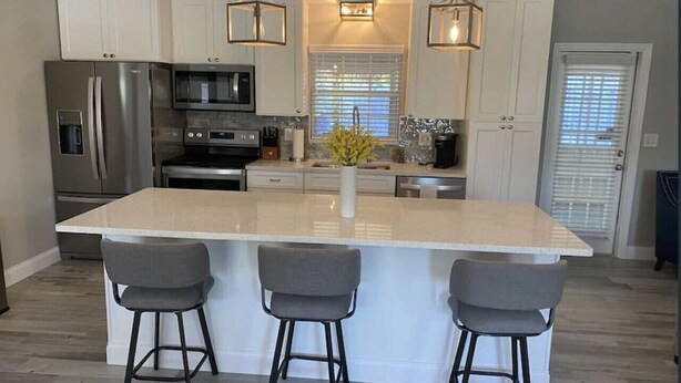 Una cocina moderna con una isla central, taburetes de bar, electrodomésticos de acero inoxidable e iluminación colgante.