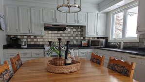Une cuisine moderne avec des meubles blancs, une table à manger en bois et un îlot central agrémenté d’une plante et d’une bouteille de vin.
